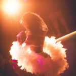 color image of Little Rock Arkansas Drag Queen Aubi Gold performing in a yellow top and white feathered wings at Diamonds and Pearls at Club Sway in orange and red tone casts