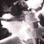 black and white image of of Little Rock Arkansas Drag Queen Aubi Gold performing in a yellow top and white feathered wings at Diamonds and Pearls at Club Sway while holding a microphone
