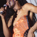 color image of Little Rock Arkansas Drag Queen Aubi Gold performing in a yellow top and white feathered wings at Diamonds and Pearls at Club Sway in a yellow skirt and top with a microphone introducing the show host Envy Hart