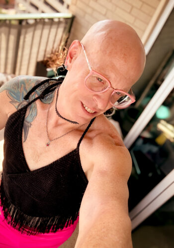 selfie of Little Rock Queer photographer Gynger in Little Rock Arkansas wearing a pink midi pencil skirt and a backless crochetted halter top with tassles and pink glasses