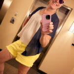 Queer photographer Gynger St Clair from Little Rock Arkansas poses in yellow shorts and a bright smile