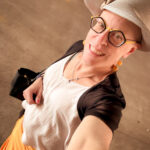 Queer photographer Gynger St Clair from Little Rock Arkansas poses while walking in a yellow pencil skirt and a sheer navy bolero