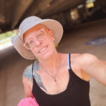 Queer photographer Gynger St Clair from Little Rock Arkansas poses to show her new hat find at Goodwill